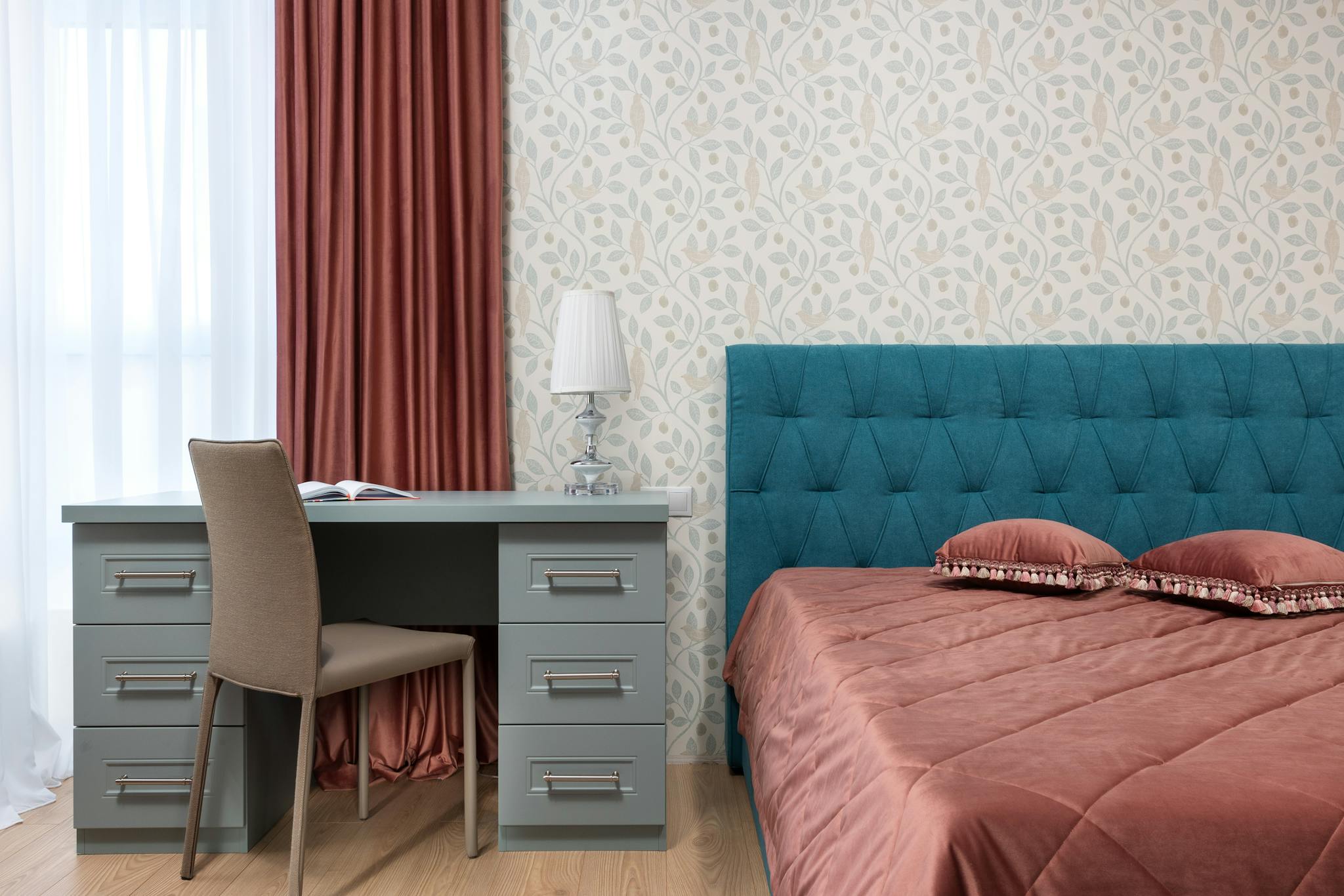 Bed with cover and cushions against lamp on table and leaf ornament on wall in light house